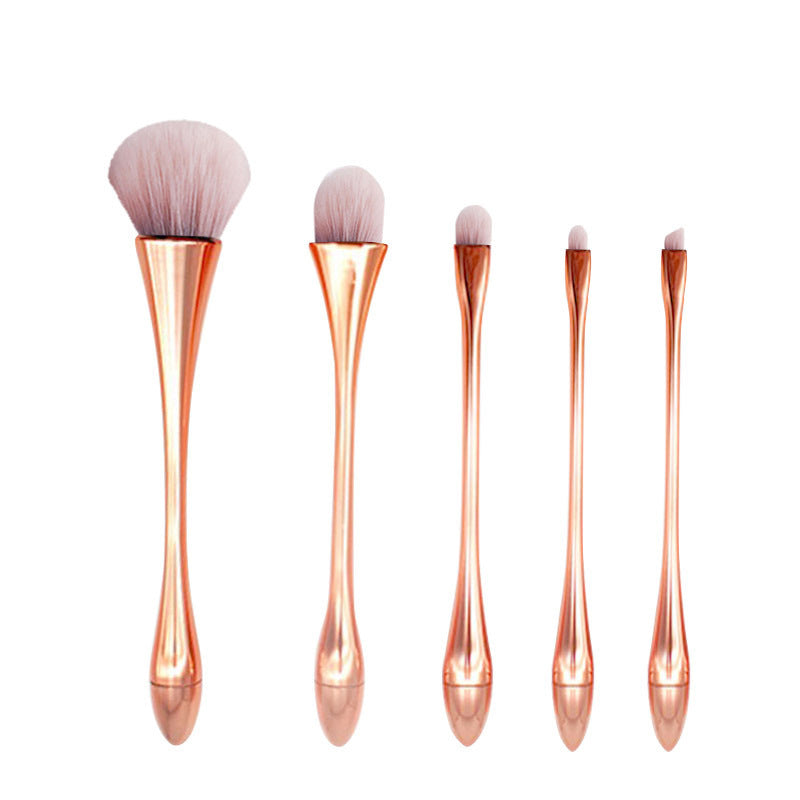 Set of five rose gold makeup brushes on a white background