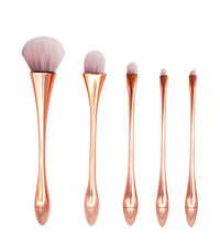 Set of five rose gold makeup brushes on a white background