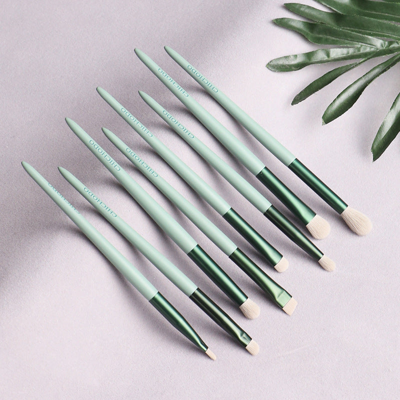 Set of green makeup brushes on a light gray background with a leafy branch.