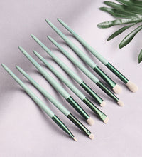 Set of green makeup brushes on a light gray background with a leafy branch.