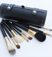 Set of makeup brushes with black and gold handles in a black leather case on a white background