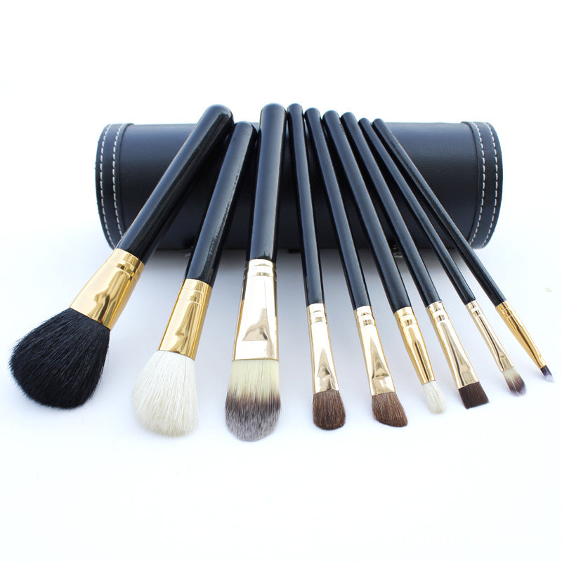 Set of makeup brushes with black and gold handles in a leather case on a white background