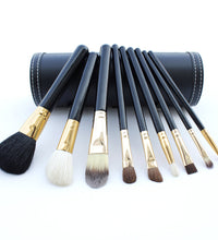 Set of makeup brushes with black and gold handles in a leather case on a white background