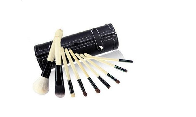 Set of makeup brushes with black handles and wooden bristles, rolled up in a black leather case on a white background.