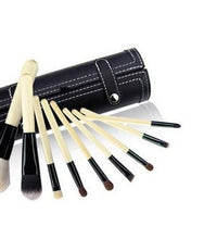 Set of makeup brushes with black handles and wooden bristles, rolled up in a black leather case on a white background.