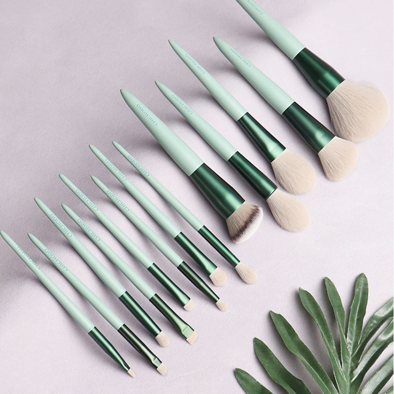 Set of makeup brushes with green and beige handles on a light gray background