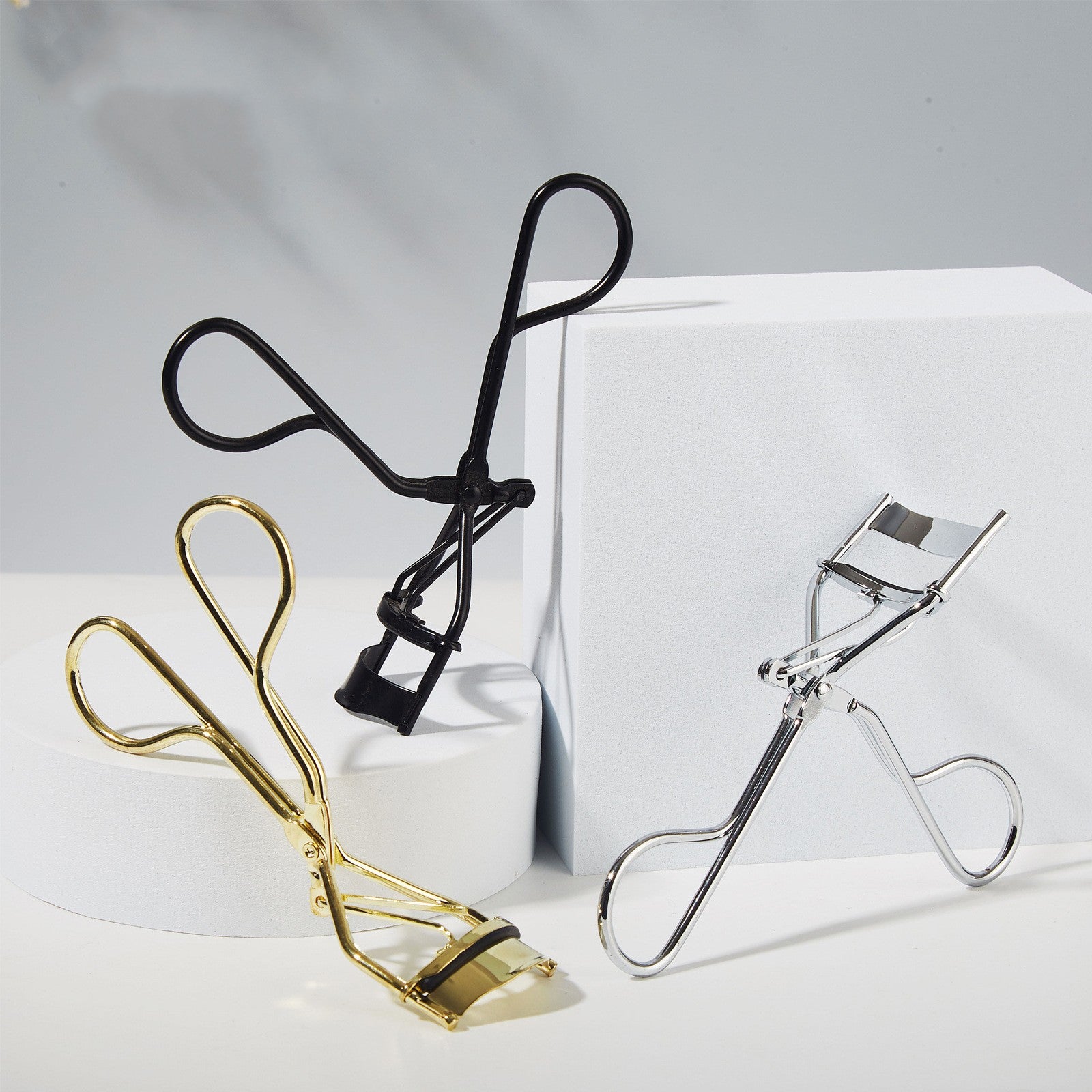 Three eyelash curlers in black, gold, and silver on a white background