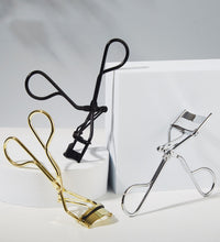 Three eyelash curlers in black, gold, and silver on a white background